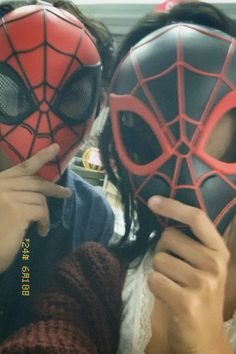 two people wearing spider man masks in front of their face and one person holding up the mask