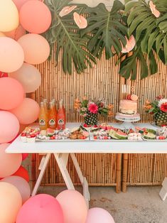 a table topped with lots of food and drinks next to a wall covered in balloons