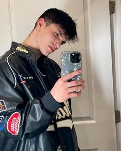 a young man wearing a leather jacket looking at his cell phone while standing in front of a door