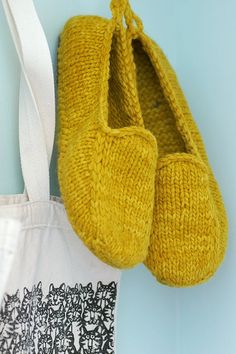 a pair of yellow knitted slippers hanging on a wall next to a bag