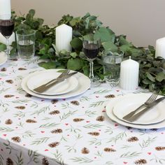 the table is set with white plates and silverware, candles, and greenery