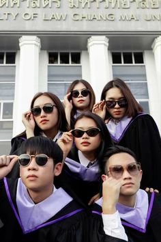 a group of young people standing in front of a building wearing graduation gowns and sunglasses