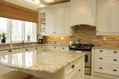 a kitchen with white cabinets and marble counter tops