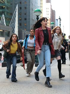 four women walking down the street in high rise jeans and jackets, with one woman holding an umbrella