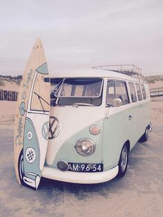 an old vw bus parked on the beach with a surfboard