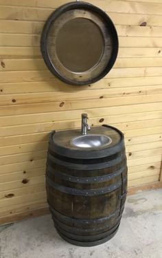 a wooden barrel sitting next to a sink on top of a cement floor in front of a wood paneled wall