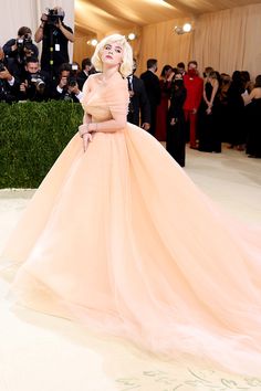 lady in an orange gown standing on the white carpet with cameras around her and people taking pictures