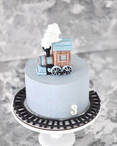 a blue cake with a wooden train on it's top and the number 3