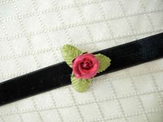 a pink rose is sitting on top of a black piece of fabric with green leaves