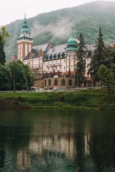 a large building sitting on top of a lush green hillside next to a lake and forest