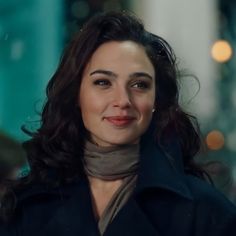 a close up of a person wearing a black coat and smiling at the camera with blurry lights in the background