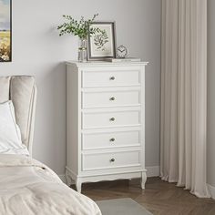 a white dresser sitting next to a bed in a bedroom under a painting on the wall