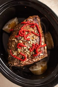 a piece of meat with red writing on it in a crock pot next to potatoes