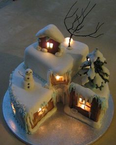 a three tiered cake with lit candles in the middle and snow covered houses on top