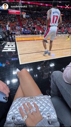 a woman sitting on top of a basketball court next to a man holding a cell phone