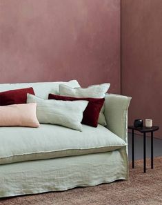 a couch with several pillows on it in front of a pink wall and side table