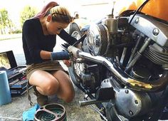 a woman working on a motorcycle in the street