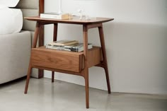 a nightstand table with books on it next to a white couch and bed in the background