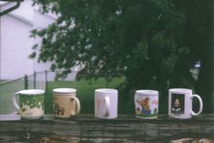 five coffee mugs are lined up on a wooden table in front of a tree