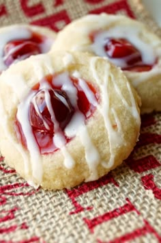 three cookies with white frosting and jelly on top sitting on a red checkered cloth