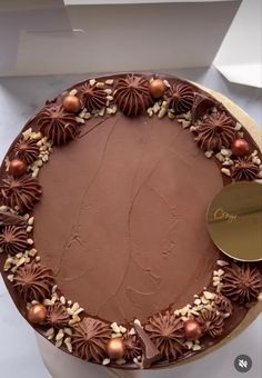 a cake with chocolate frosting and nuts on top sitting on a table next to a white box