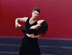 a man and woman dance together in front of a red wall