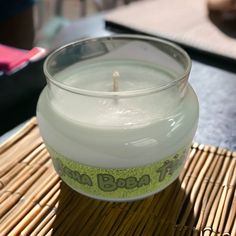 a white candle sitting on top of a bamboo mat next to a glass container filled with liquid