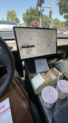 two cups of coffee sit in front of a computer monitor on the dashboard of a car