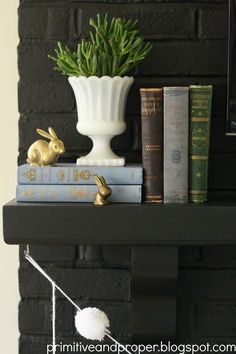 some books are sitting on a shelf near a potted plant and two bunny figurines