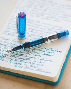 a blue pen sitting on top of an open notebook next to it's writing