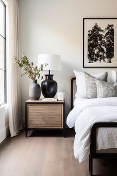 a bedroom with white bedding and two black vases on the nightstand next to it