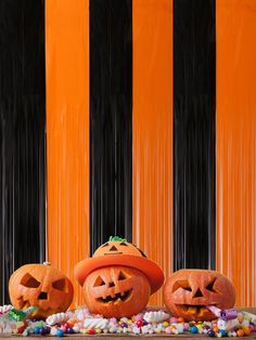 two jack - o'- lanterns with candy in front of an orange striped wall