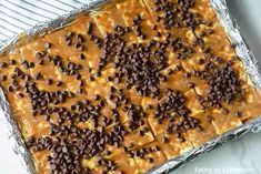 a pan filled with chocolate chips and peanut butter cheesecake bars on top of aluminum foil