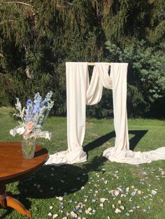 a wooden table sitting on top of a lush green field next to a white drape