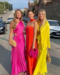 three beautiful women standing next to each other in front of parked cars on the street