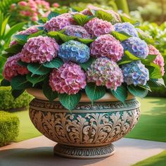 a large vase filled with purple and blue flowers on top of a stone slab in a garden