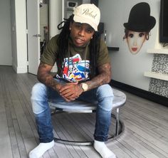 a man with dreadlocks sitting on a stool in a room wearing a hat