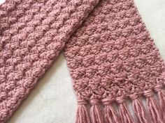 a pink crocheted scarf laying on top of a white blanket