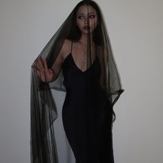 a woman in a black dress is holding her veil over her head and looking at the camera