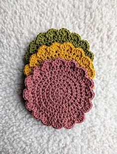 four crocheted coasters sitting on top of a white blanket in different colors