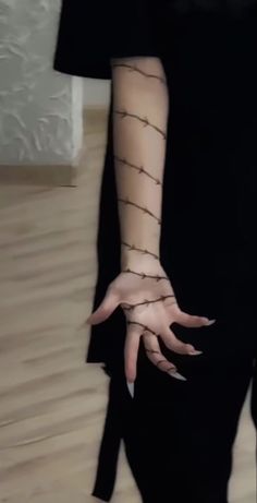 a woman's hands with black nails and mesh on her arm, standing in front of a white wall