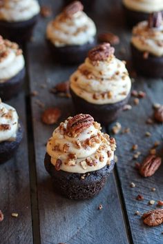 chocolate cupcakes with white frosting and pecans scattered around on a wooden table