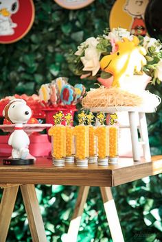 a table topped with lots of food and candles next to a wall covered in green leaves