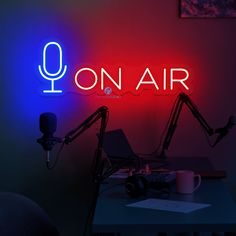 there is a neon sign that says on air next to a desk with a laptop and microphone