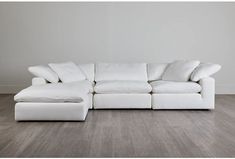 a large white sectional sofa with pillows on the back and footrests, in an empty room