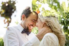 a man and woman are smiling together in front of some trees with their heads close to each other