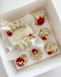 a white box filled with cupcakes covered in frosting and red flowers next to each other