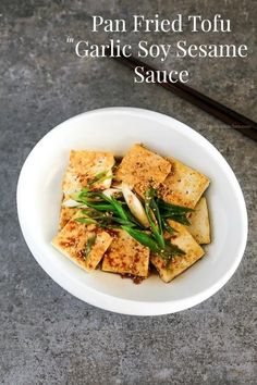 pan fried tofu with garlic soy sesame sauce in a white bowl next to chopsticks