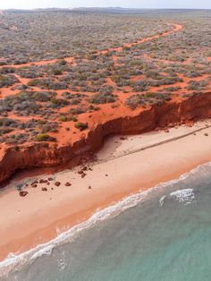 an aerial view of the beach and ocean with red sand, blue water and green vegetation