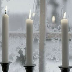 three lit candles sitting in front of a window with frost on the windowsills